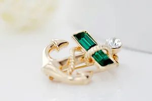 Close-up of golden anchor brooch with emerald green crystals and nautical rope detail