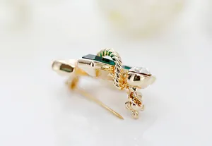 Detailed close-up of gold nautical anchor brooch with green crystal and twisted rope texture