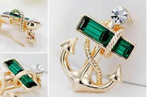 Macro detail of nautical anchor brooch with emerald crystals and gold rope texture