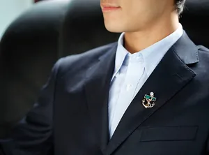 Golden anchor brooch with emerald green crystal on a navy blue suit lapel