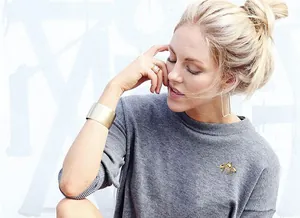 Lifestyle view of a golden bee brooch and matching gold jewelry on a grey knit sweater