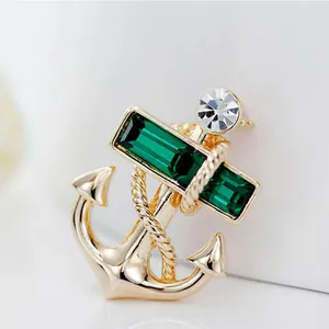 Golden anchor brooch with emerald green crystals and nautical rope design on white background