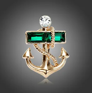 Gold anchor brooch with emerald green gemstones and crystal detail on dark background