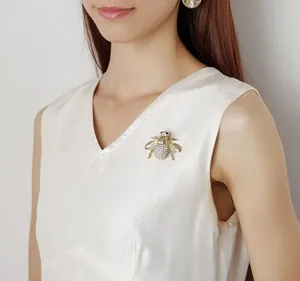 Exquisite gold bee brooch with white crystals shown on a model's white V-neck top
