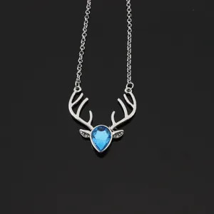 Macro detail of silver deer pendant with blue teardrop crystal on black mirror surface