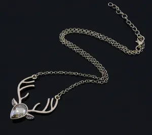 Detail of gold reindeer necklace with pear-shaped crystal on reflective black background