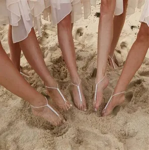 Close-up of five women wearing silver rhinestone T-strap barefoot sandals on a sandy beach