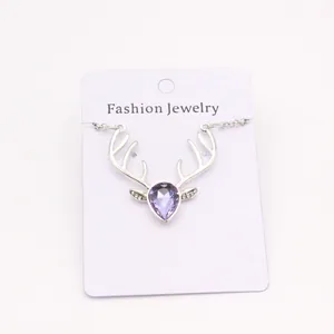 Close-up of silver reindeer antler necklace with a purple teardrop gem on display card