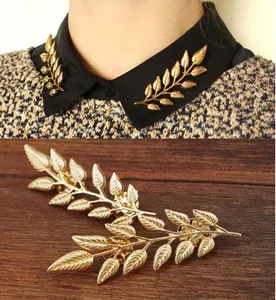 Close-up of golden leaf-shaped collar pins with detailed veins on black fabric and wood