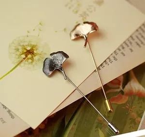 Detailed view of silver and gold ginkgo leaf pins with realistic texture on a vintage postcard