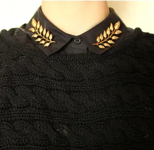 Close-up of golden leaf collar pins on a black shirt showing detailed texture and symmetry