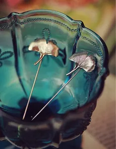 Detailed close-up of gold and silver ginkgo leaf brooches with brushed metal texture