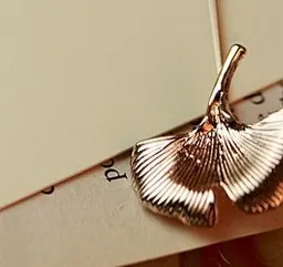 Elegant rose gold ginkgo leaf brooch featuring fine radial textures on vintage paper
