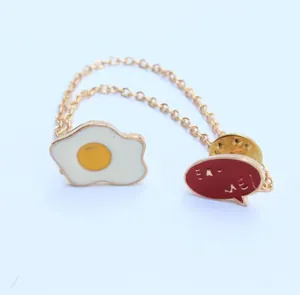 Detalle de broches de esmalte con huevo frito y texto Eat Me unidos por cadena