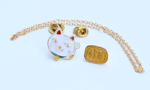 Vista detallada de los broches de esmalte Maneki Neko y moneda con cadena dorada