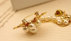 Détail d'une broche dorée élégante avec perles blanches et fine chaîne à pompon sur papier