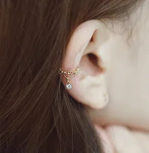 Primer plano de un pendiente de clip dorado con patrones calados y colgante de gota de circón