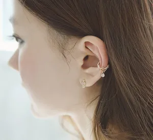 Detalle de ear cuff dorado vintage con patrones huecos y gota de agua de circón