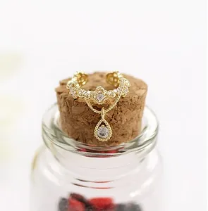 Detalle de clip de oreja dorado en forma de gota con circones sobre frasco de cristal