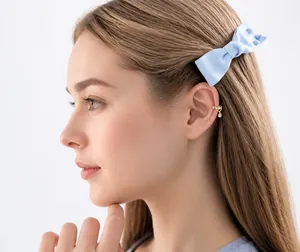 Detalle de un ear cuff de corazón dorado y un clip de pelo con lazo azul y tachas