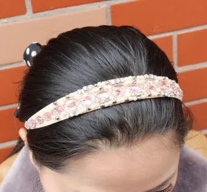 Detail of handmade headband with pink crystal hearts and white faux pearls on beige fabric
