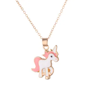 Gros plan d'un collier doré avec pendentif licorne en émail rose et blanc sur fond blanc