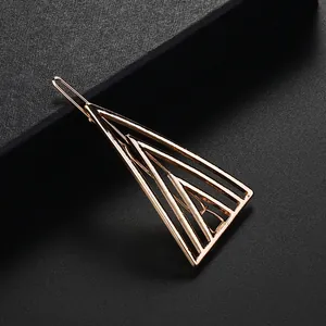 Minimalist gold geometric triangle hair clip with hollow nested design on a textured surface