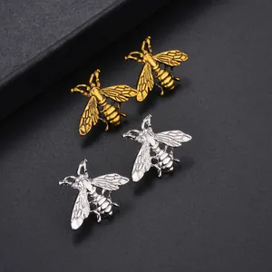 Detalle macro de broches de abeja realistas en acabados oro y plata sobre fondo oscuro