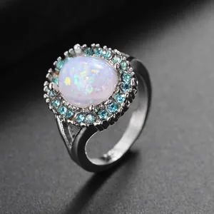 Primer plano de anillo de opalo blanco ovalado con halo de circon blue y banda de plata