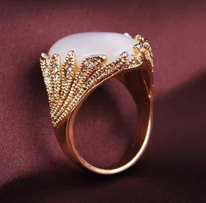 Nahaufnahme eines Rings mit ovalem weißem Edelstein und Goldband im Federdesign
