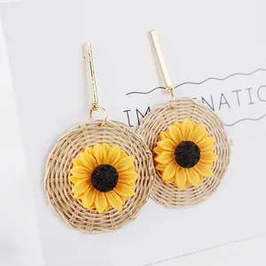 Detail of sunflower drop earrings with woven straw base and golden metal ear hooks