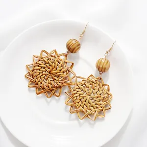 Detail view of woven rattan sunflower drop earrings with natural wood beads and gold hooks