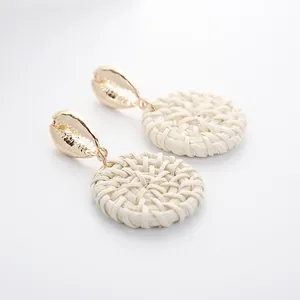 Detailed macro view of bohemian shell earrings with white woven disk and gold accents
