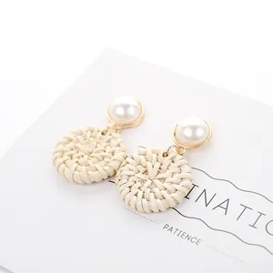 Detailed macro view of woven rattan earrings with white imitation pearl and gold metal stud