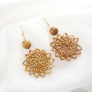 Close-up of star-shaped woven rattan earrings with wooden beads and gold hooks