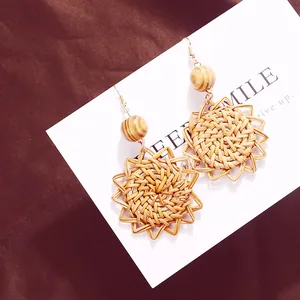 Detail view of sunflower woven rattan drop earrings with a wooden bead on brown silk