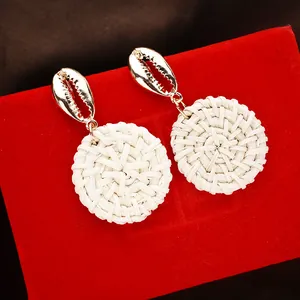 Detail of bohemian shell earrings with gold conch stud and white woven rattan drop