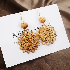 Handwoven sunflower-shaped rattan earrings with wooden beads and golden hooks on card