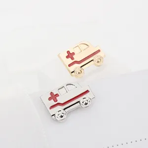 Detalle de pines de ambulancia en esmalte dorado y plateado con emblemas de cruz roja en blanco