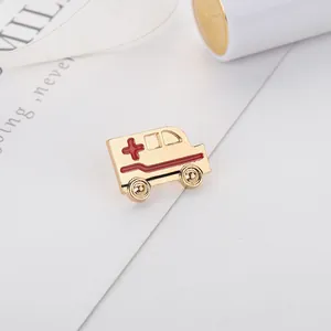 Detalle de un broche de ambulancia dorado con esmalte rojo e icono de cruz médica