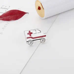 Primer plano de pin de ambulancia de esmalte plateado con cruz roja sobre papel blanco