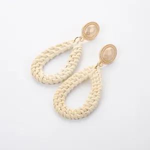 Macro detail of bohemian waterdrop earrings featuring textured metal disks and woven raffia