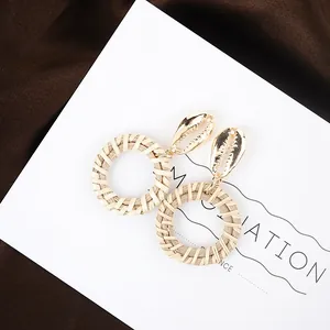 Detail of bohemian shell gold metal stud earrings with handwoven round rattan pendants
