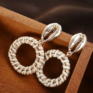 Close-up of bohemian earrings featuring golden seashell studs and woven rattan circles