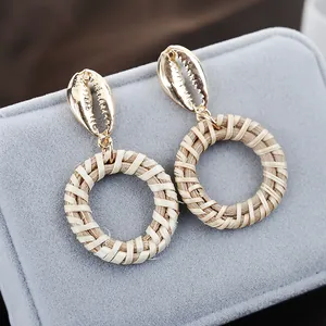 Detail of bohemian shell stud earrings with natural woven rattan texture and gold finish