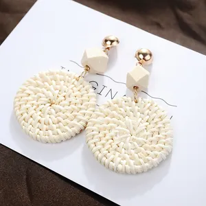 Detail of bohemian geometric woven rattan earrings with wood bead and gold stud