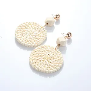 Detail of round cream rattan woven earrings with gold stud and geometric wood link