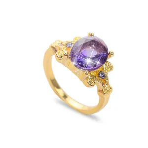 Bague dorée avec pierre précieuse violette ovale et texture lave sur fond blanc