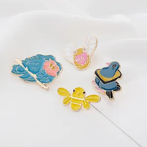 Detalle de cuatro broches de esmalte con aves y abejas coloridas sobre un fondo de tela blanca