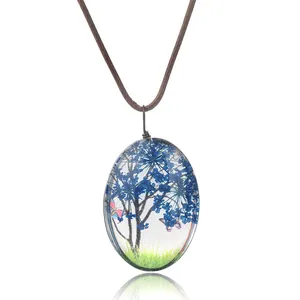 Détail du pendentif ovale en résine avec fleurs séchées bleues et petit papillon